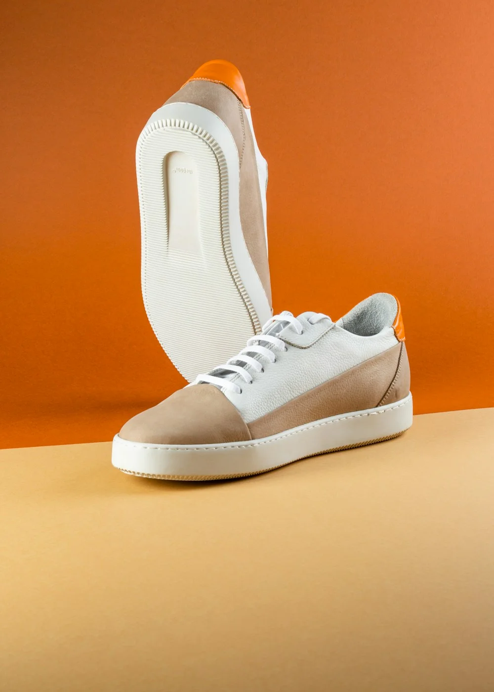 White and tan sneakers thoughtfully styled against a warm amber studio backdrop